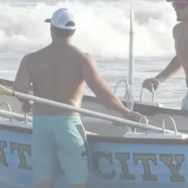 Man standing in water with ocean racing row boat.